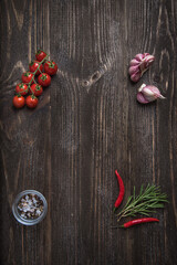 Fototapeta na wymiar Wooden background with vegetable decor: cherry tomatoes, garlic, rosemary and chilli peppers