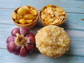 Garlic: whole pickled, cut into thin strips, garlic paste and paste in wooden bowls and a bulb of fresh garlic, isolated on a wooden table, top view, copy space. A great ally of health.