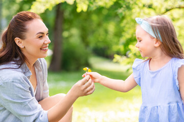 family, motherhood and people concept - happy mother with little daughter with flowers at summer...