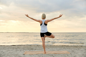 Fototapeta premium fitness, sport, and healthy lifestyle concept - woman doing yoga tree pose on beach over sunset