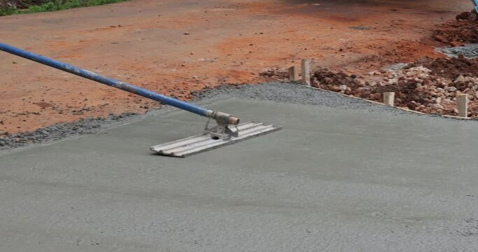 Worker is holding a steel fresno concrete trowel and smoothing plastering over freshly poured concrete that is wet in construction zone