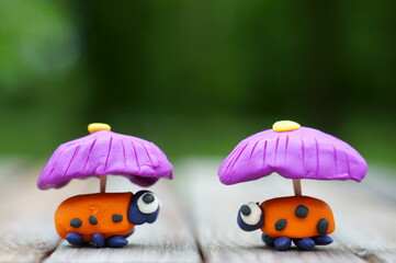 Two toy ladybugs with umbrellas. Toys made of plasticine. Rainy weather.