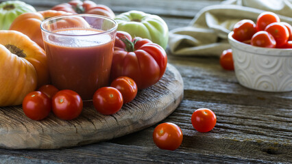 Tomato juice surrounded by heirloom and cherry tomatoes, on a rustic board.
