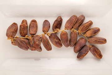One branch with dry sweet dates on a white ceramic plate, close-up, top view.