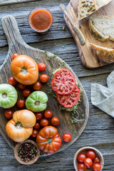 Several tomatoes on a rustic board with an open tomato sandwich.
