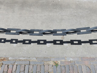 chain with shadow forming the partition between the sidewalk and the road