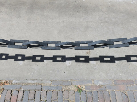 chain with shadow forming the partition between the sidewalk and the road