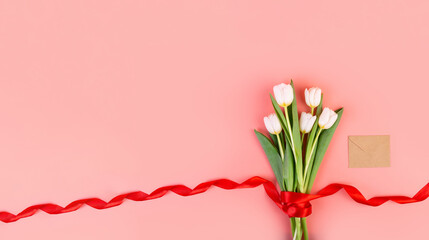 Flowers are white tulips, flatlay. A beautiful bouquet tied with a red ribbon and an envelope isolated on a pastel pink background. object for decoration for women's day, mother's day, anniversary.