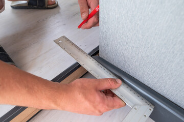 Installing a plinth in the room, measuring the required length using a square and a ruler, a gray...