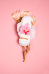 Plastic doll with sanitary napkin with orchid flower on it  on pink background.