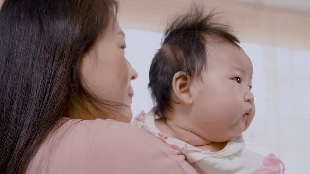 4K, Close Up is a 3-month-old newborn Asian girl who her mother is holding. A single mother is holding her newborn baby by soothing her to sleep. in the bedroom of the house. Family and Healthy.