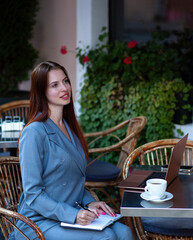 Beautiful confident woman. Woman on the street at the table . Business consultant, to note down, to make notes. Business meeting. Woman with notebook. Business look.