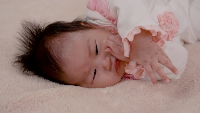 4K,  Asian newborn baby girl 3 months old is lying on the bed with her hands clasped and releasing and covering her face happily while waiting for her mother to take care of her.