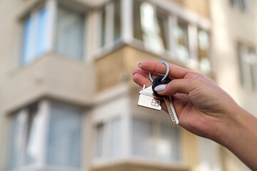 key to the house in the hands of a woman against the background of a new apartment building.