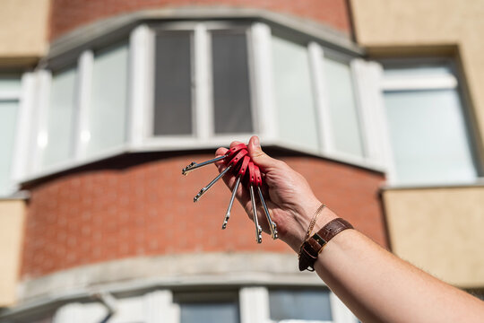 Men's Hands Holding Key With A Keychain In Shape Of A House On  Background Of Cool House.