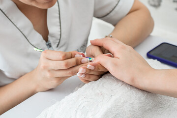 latina manicurist working at home, cleaning a girl's nails with the cuticle pusher. woman learning the art of manicuring, painting and decorating nails.