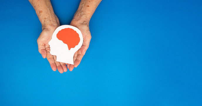 Top view of head with a brain made from paper on the palm senior woman over a blue background