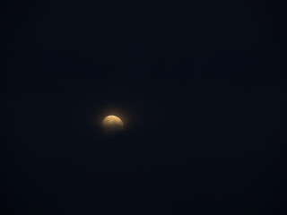 Moon, part obscured by cloud, hangs in starless night sky. Mystical in the darkness.