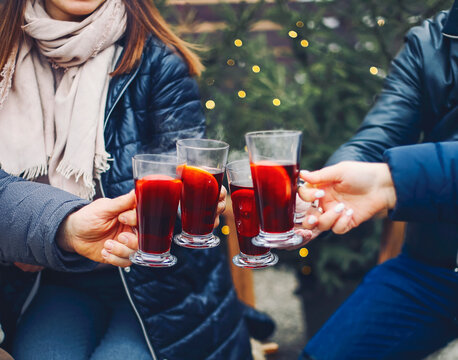 Friends drinking delicious mulled wine at party. Shot of a group of cheerful young friends having fun and enjoying hot drink on the Christmas market at an evening party. Close up