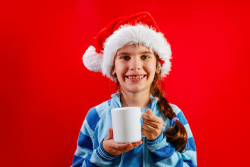 Cute child girl in santa hat for Christmas on a red background. Mock up cup in hand. Holidays concept. Holidays sales and shopping.