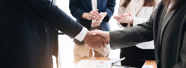 Two  business men shaking hands while their colleagues applauding in the background