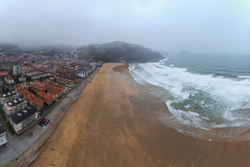 Scenic coastal town with red roofed buildings near wide sandy beach and wavy sea