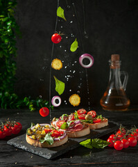Ciabatta toasts with tomatoes, cucumber, onion, olives, lettuce, cheese, pesto sauce on the plate with food levitation
