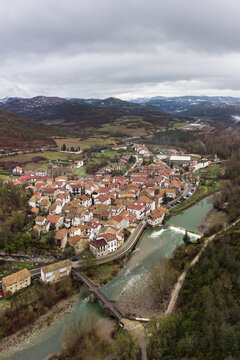 Red roofed houses near river in mountainous countryside under gloomy sky
