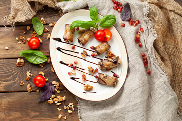 A traditional dish of eggplant rolls in a plate. On a wooden table.