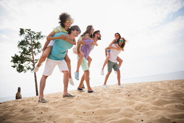 Full length portrait of group excited positive people piggyback walking sand beach have good mood...