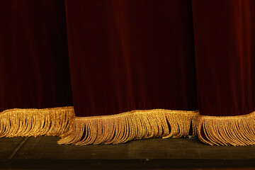 Theatrical dark red velvet curtain with golden fringe. Texture background for design.
