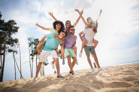 Full size photo of group overjoyed carefree people piggyback rejoice walk sand beach free time outside