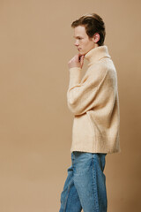 a young, handsome, thoughtful guy is standing in a warm, long beige autumn sweater on a plain background.