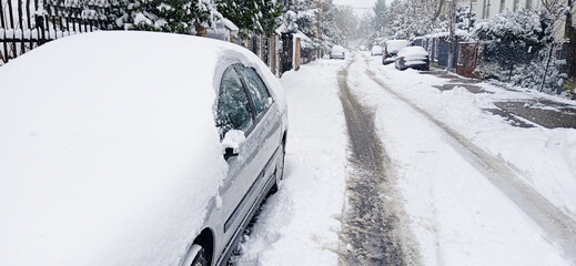 A snowy street and a car under a layer of snow