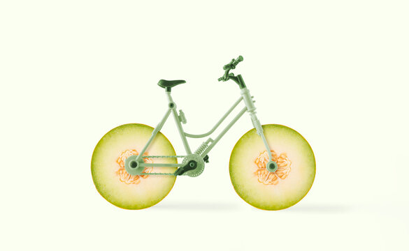 Minimal abstract summer fruit scene with bicycle with wheels made of melon slices on isolated pastel yellow background. Food delivery or agriculture concept. Creative idea of healthy organic raw food.
