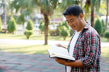 Asian man is at the park, holds book to read. Concept : Relax time, pastime, hobby. Give time for yourself to read books , magazine, novels. Reading in daily life. Education ,knowledge or  pleasure.  