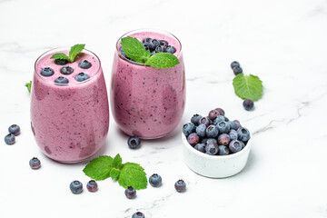 yogurt smoothies fresh blueberries in glass with mint leaf and raw beeries on blue background. Restaurant menu, dieting, cookbook recipe top view