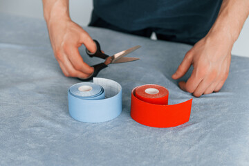 Close up view. Cutting by scissors. Professional physiotherapist is standing indoors with kinesio tape