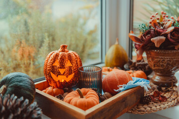 Halloween cozy mood composition on the windowsill. Lighting jack-o-lantern, decorative pumpkins,...