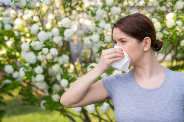 Middle-aged woman blowing her nose in a flowering garden.  - obrazy, fototapety, plakaty