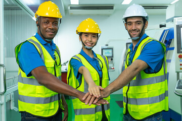 Group of young multiethnic confident male and female Engineers and Worker in safety uniform and helmet join hand together in factory. Successful business and teamwork