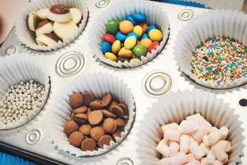 Chocolate and candy toppings for sweet desserts or cakes in paper cup cake liners on a baking tray