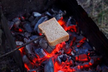 fry bread on a campfire on a camping trip, bread impaled on a stick over coals, cook brown bread on an open fire, a slice of bread fried on a fire, roast bread over hot coals