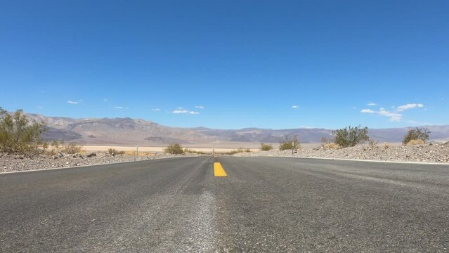 SLOW MOTION SHOT - State Route 190 crossing Panamint Valley in Death Valley National Park, California, United States. Empty desert road in Death Valley with clear blue sky.