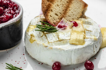 Baked camembert cheese with cranberries, basil leaves and rosemary on dark table. French cuisine....