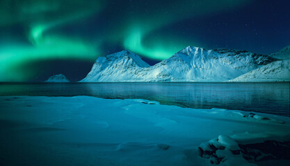 Magical aurora borealis above frozen sea coast and snow covered mountains reflected in the ocean in...