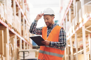 With notepad. Employee in uniform is working in the storage at daytime