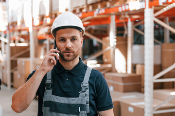 Talking by phone. Employee in uniform is working in the storage at daytime