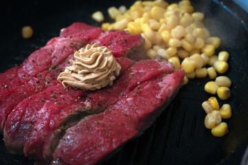 A rare reddish steak on a sizzling hot plate with corn kernels as garnish and butter on top of the steak