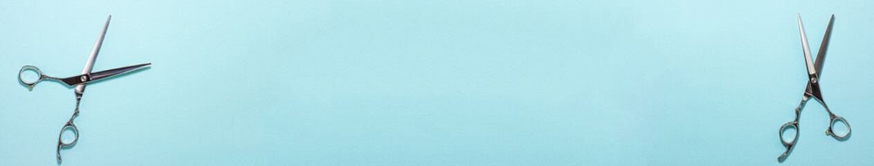 Banner flat lay of professional hair cutting shears on the left and right side on blue cyan background. Hairdresser salon equipment concept with copy space